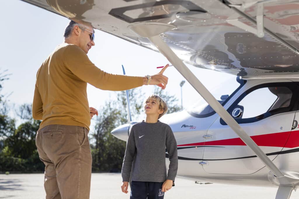A man and a child inspecting the underside of a light aircraft on a sunny day.