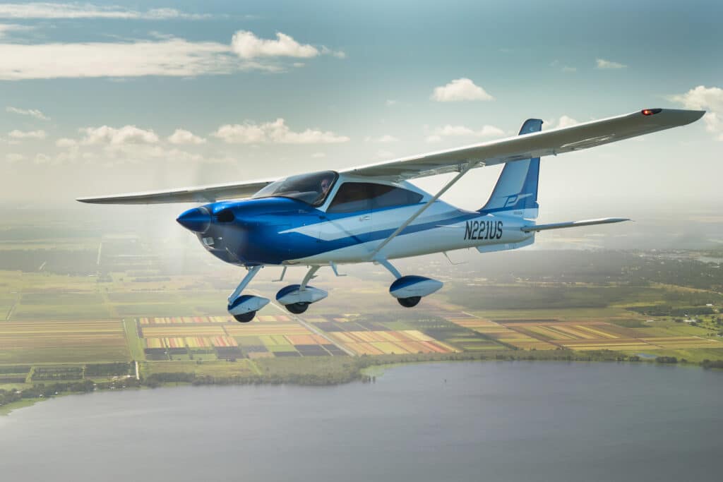Blue Cessna aircraft flying above a landscape with fields and a body of water.