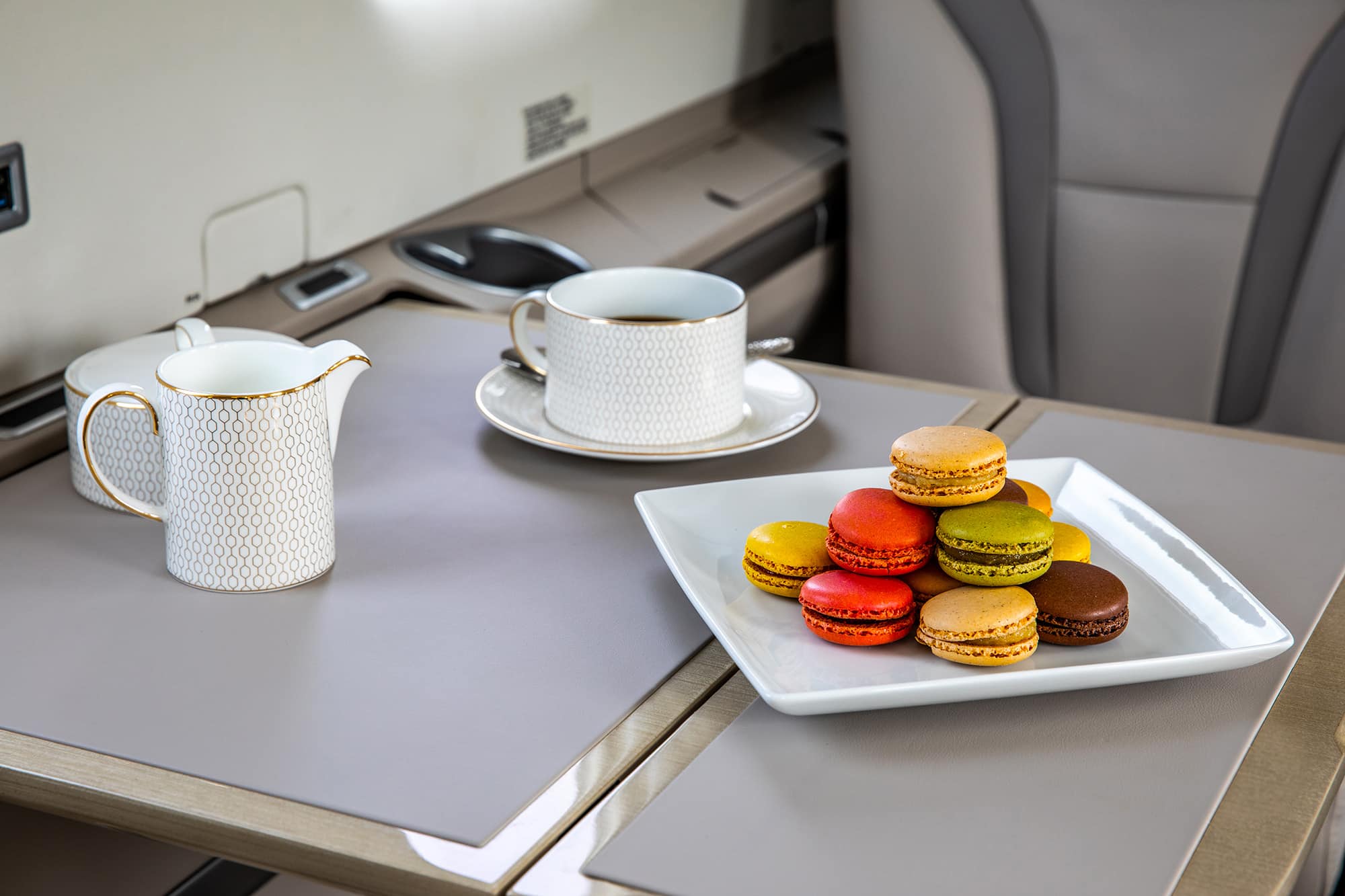 A plate of assorted macarons in various colours alongside a tea set on a table.